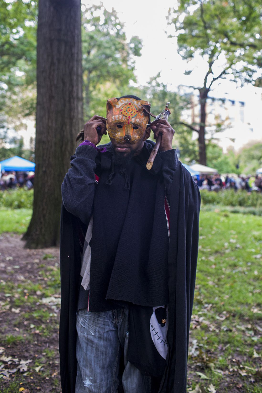 Crow holds a healing wand made of wood and smudge feather fan as he puts on his jaguar mask during the Pagan Pride Festival in Washington Square Park on Saturday, October 1, 2016. Crow says, “One of the most important things, before you become a shaman or medicine man, or whatever you have to heal yourself before you can heal others and I’m still working on that for myself.”<br>